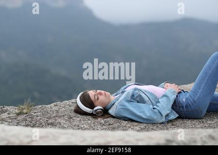 Sad teen listening to music wearing headphones alone in the mountain Stock Photo