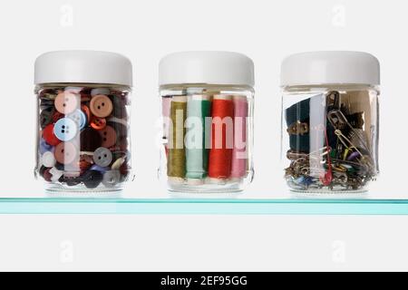 Close-up of buttons and safety pins with thread spools in three different jars Stock Photo