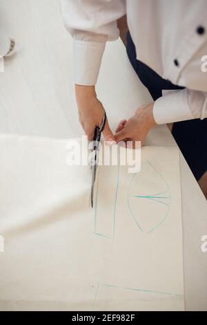 Close up. hands woman Tailor working cutting a roll of fabric on which she has marked out the pattern of the garment she is making with tailors chalk. Stock Photo