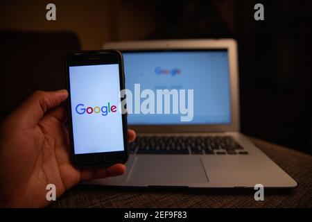 Close up of Google Logo on the iPhone display stands in front of a macbook with the desktop version.Google's the most used search engine in the world Stock Photo
