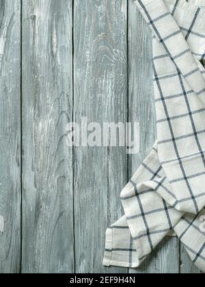 Gray wooden table with linen kitchen towel or textile napkin flat lay. Blue tablecloth on old gray wood tabletop. Copy space for text. Can use as mock up for design. Vertical. Stock Photo