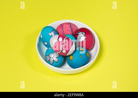 Multicolored Easter eggs in a white plate on a yellow background. Patterns and designs on colored dyed eggs. Stock Photo