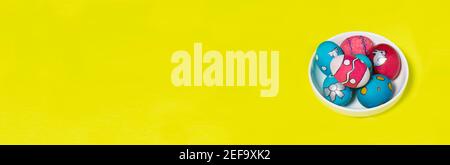 Multicolored Easter eggs in a white plate. Patterns and designs on colored dyed eggs. Banner on yellow background with place for text. Stock Photo