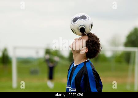 Side profile of a soccer player balancing a soccer ball on his forehead Stock Photo