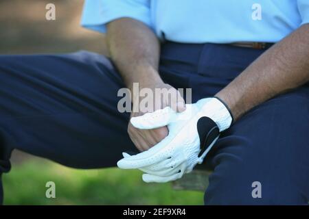 Mid section view of a man sitting on the bench wearing a golf glove Stock Photo