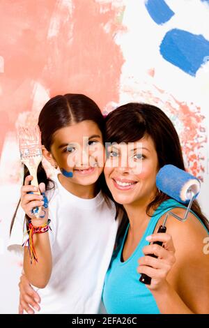 Portrait of a young woman holding a paint roller with her daughter holding a paintbrush Stock Photo