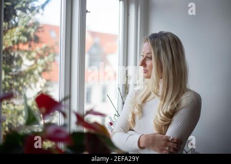 a beautiful girl looks out the window during a cold winter day in quarantine during the coronavirus pandemic Stock Photo