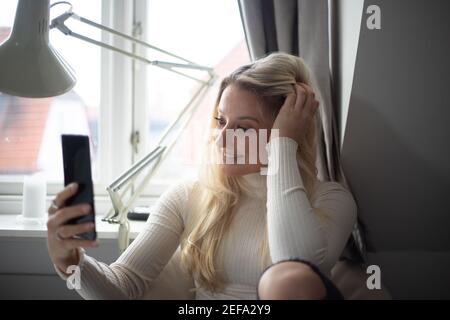 Attractive girl takes a selfie with the front camera of her smartphone at home Stock Photo