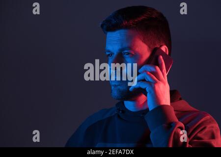 a man illuminated with colored neon lights talks on the phone Stock Photo