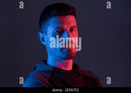 a man illuminated with colored neon lights looks at the camera Stock Photo