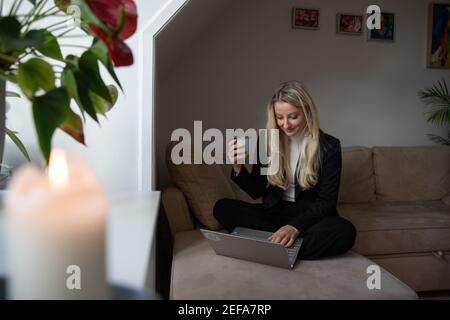 A relaxed business woman working from home sitting on the couch with a cup of coffee in her hand Stock Photo
