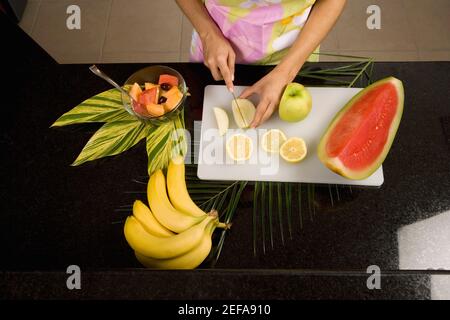 Mid section view of a woman cutting a green apple on a cutting board in the kitchen Stock Photo