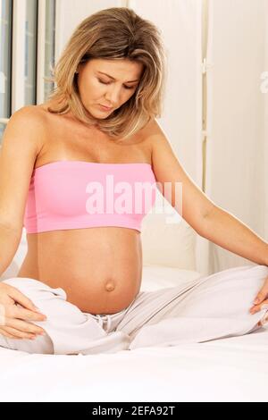 Pregnant woman sitting on the bed with her hands on her knees Stock Photo