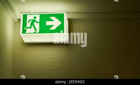 Green glowing emergency exit sign on wall in the house as a notice sign Stock Photo