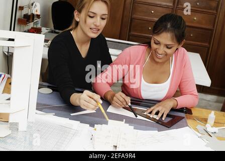 Two female architects drawing a blueprint and smiling Stock Photo