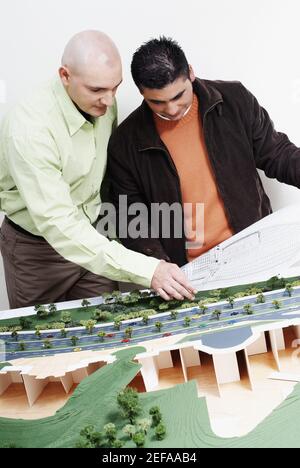 Two architects standing near a model and discussing a blueprint Stock Photo