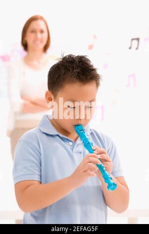 Close up of a schoolboy playing a flute with his female teacher standing in the background Stock Photo