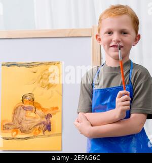 Portrait of a schoolboy standing in front of his painting in a classroom Stock Photo