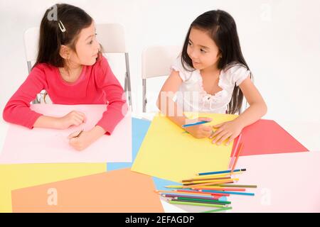 Two schoolgirls drawing in an art class and looking at each other Stock Photo