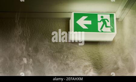 Green glowing emergency exit shows escape route in case of fire with smoke in the house Stock Photo