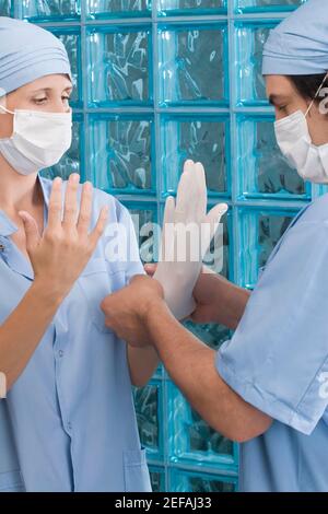 Male surgeon adjusting a surgical glove of a female surgeon Stock Photo