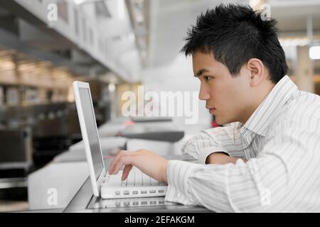Side profile of a young man using a laptop at an airport Stock Photo