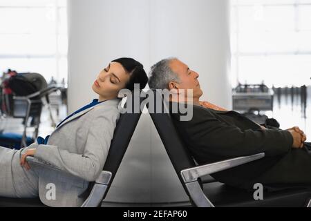 Side profile of a businessman and a businesswoman sleeping on chairs at an airport Stock Photo