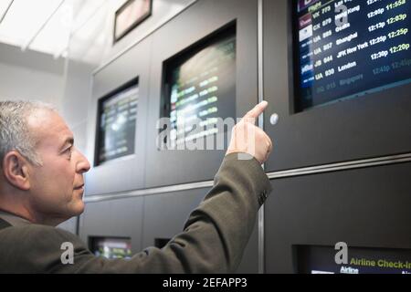 Side profile of a businessman pointing at an arrival departure board in an airport Stock Photo