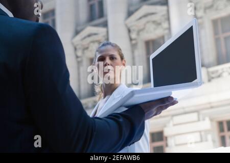 Side profile of a businessman using a laptop with a businesswoman standing in front of him Stock Photo