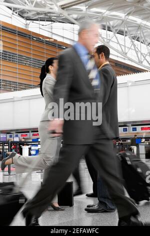 Two businessmen and a businesswoman walking at an airport Stock Photo