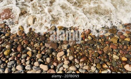 Waves wash water over wet stones and pebbles on the beach Stock Photo