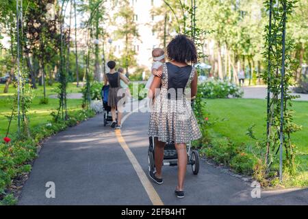 Two young mothers pushing strollers in park. Women in the park walking with strollers Stock Photo