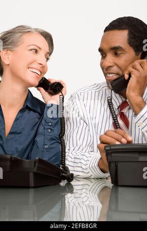 Businessman and a businesswoman talking on landline phones Stock Photo