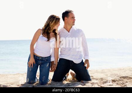 Mid adult man and a young woman kneeling with holding hands on the beach Stock Photo