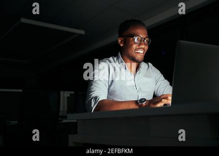 Smiling african young businessman working overtime in the office to finish the project within the deadline Stock Photo