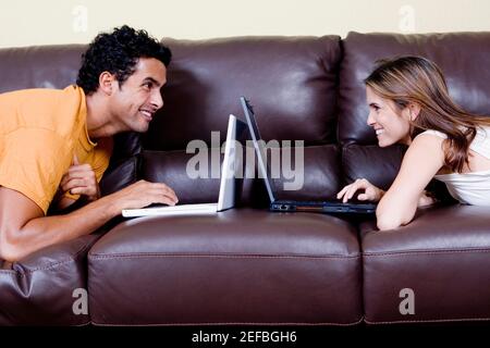Side profile of a young couple lying on a couch and using laptops Stock Photo