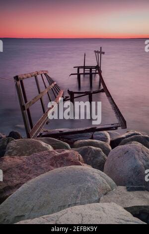 Old wooden jetty falling into the sea during lovely gradient sunset. Stock Photo