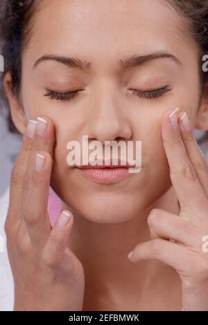 Close-up of a young woman applying moisturizer on her cheeks Stock Photo