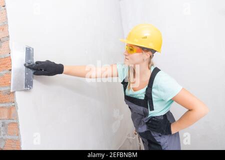 Female molar plasterer worker prepares the wall for applying plaster and leveling surface with spatula. Stock Photo