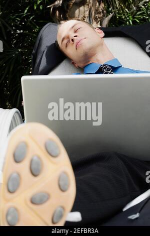 Businessman sleeping on a lounge chair with a laptop on his lap Stock Photo