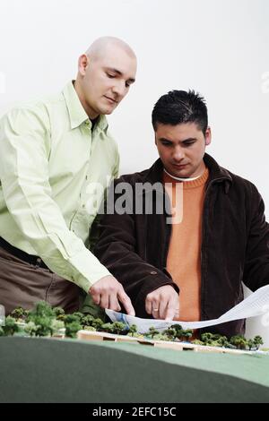Two architects standing near a model and discussing a blueprint Stock Photo