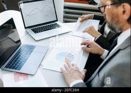 Close-up of business people doing paperwork, learning financial graphs and diagrams. .Senior adult employess sitting at the desk in modern office, working with documents for the project Stock Photo