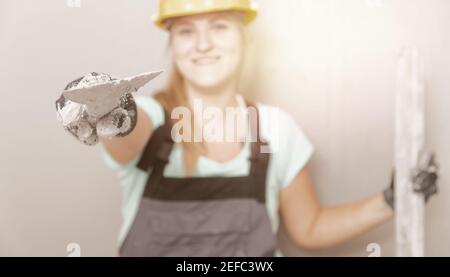 Happy builder woman construction worker in yellow helmet on background of gray wall, copy space. Stock Photo