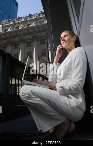 Side profile of a businesswoman talking on a mobile phone and using a laptop Stock Photo