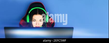 The gamer sits on a gaming chair and plays computer games. The player has green headphones on his head. Stock Photo