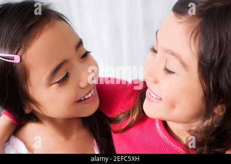 Two schoolgirls looking at each other and smiling in a classroom Stock Photo