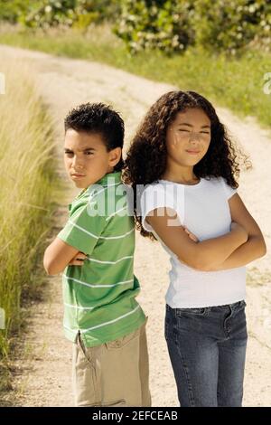 Portrait of a boy and a girl standing back to back with their arms crossed Stock Photo