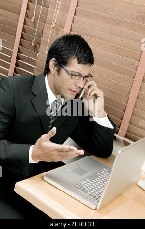 High angle view of a businessman sitting in front of a laptop using a mobile phone Stock Photo