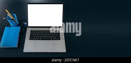 Panoramic photo of the desktop. On the table is a laptop with a blank white screen, a notepad and a stationery. Copy space Stock Photo
