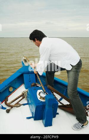 Side profile of a mid adult man pulling a chain in a boat Stock Photo